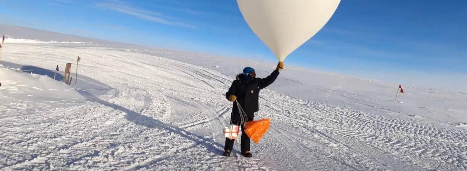 A person in heavy winter gear launches a weather balloon in a snow and ice filled landscape.