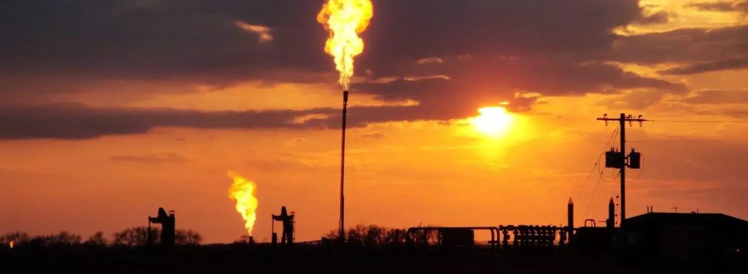 Methane flaring from a well site in front of an orange sky
