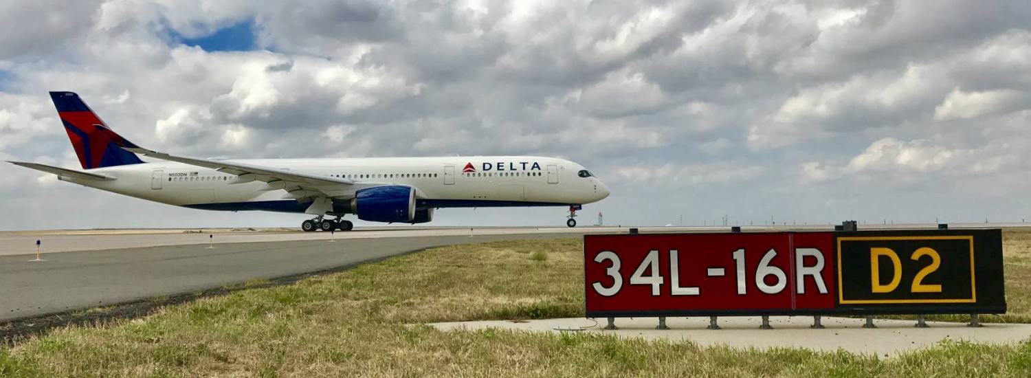 Delta airplane on airport runway with runway marker in foreground