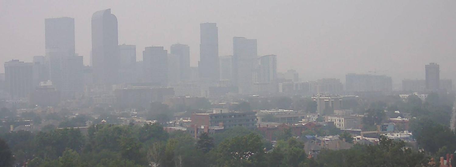 Smoky view of Denver skyline shows outlines of tall buildings almost obscured by haze