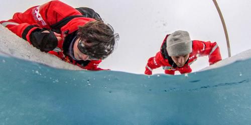 Researchers in heavy snowsuits peer below into a hole in the ice