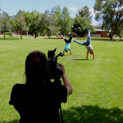 A student films other children doing cartwheels while a mentor looks on.