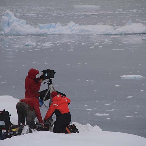 3 people and a camera on a floating ice sheet with water in the background