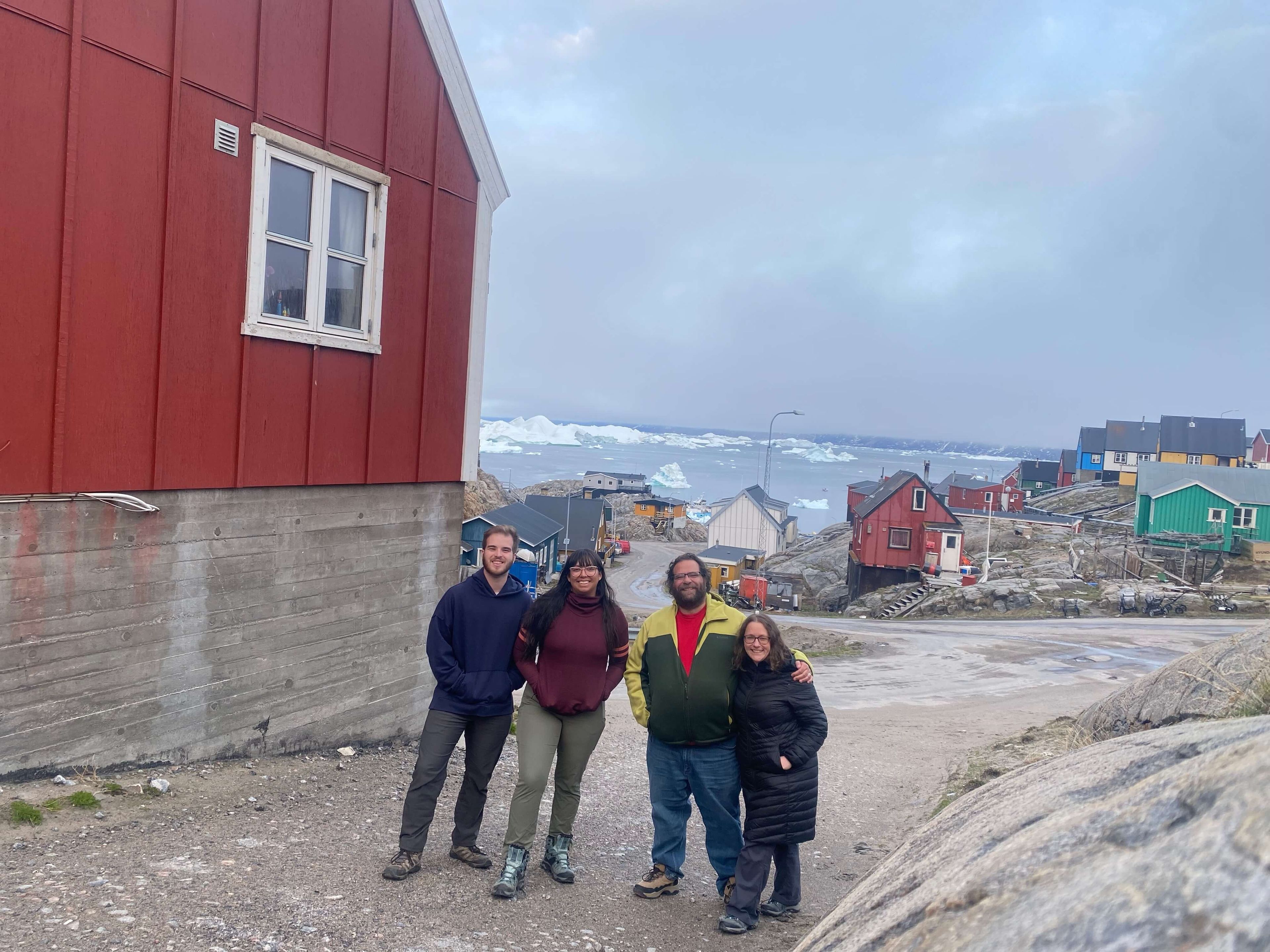 four people posing by a red building