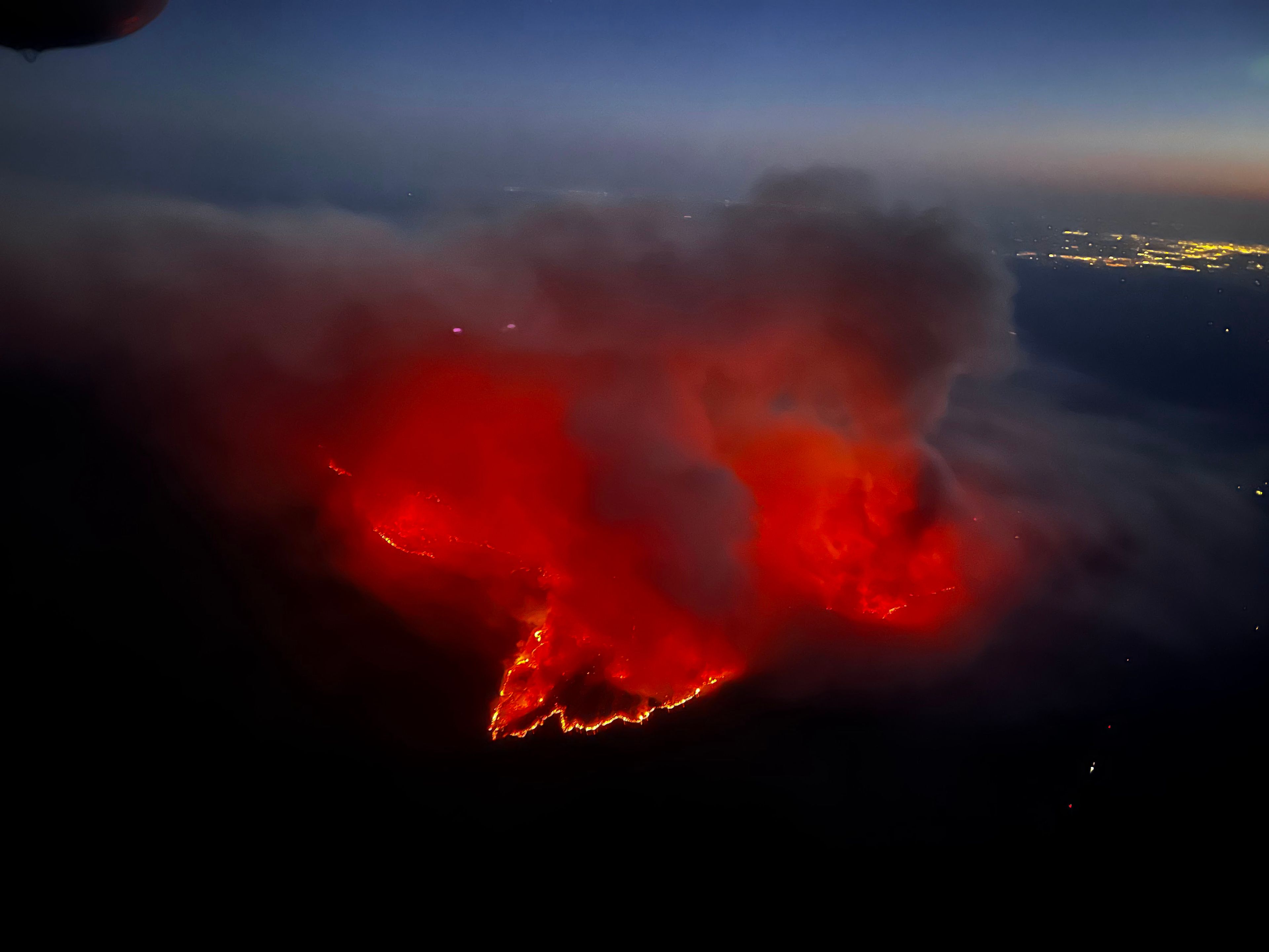 A wildfire at night, seen glowing red among the surrounding hills. 