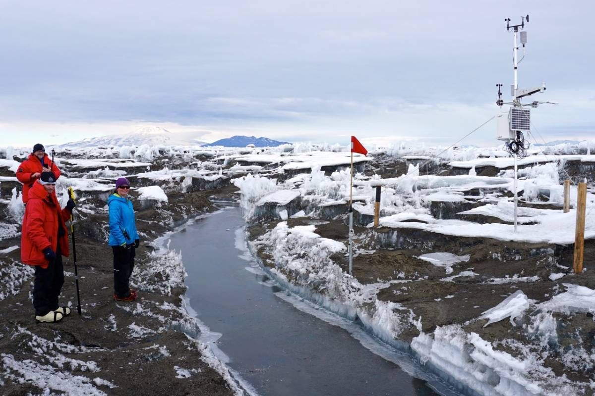 Three people in winter gear stand near a meltwater stream