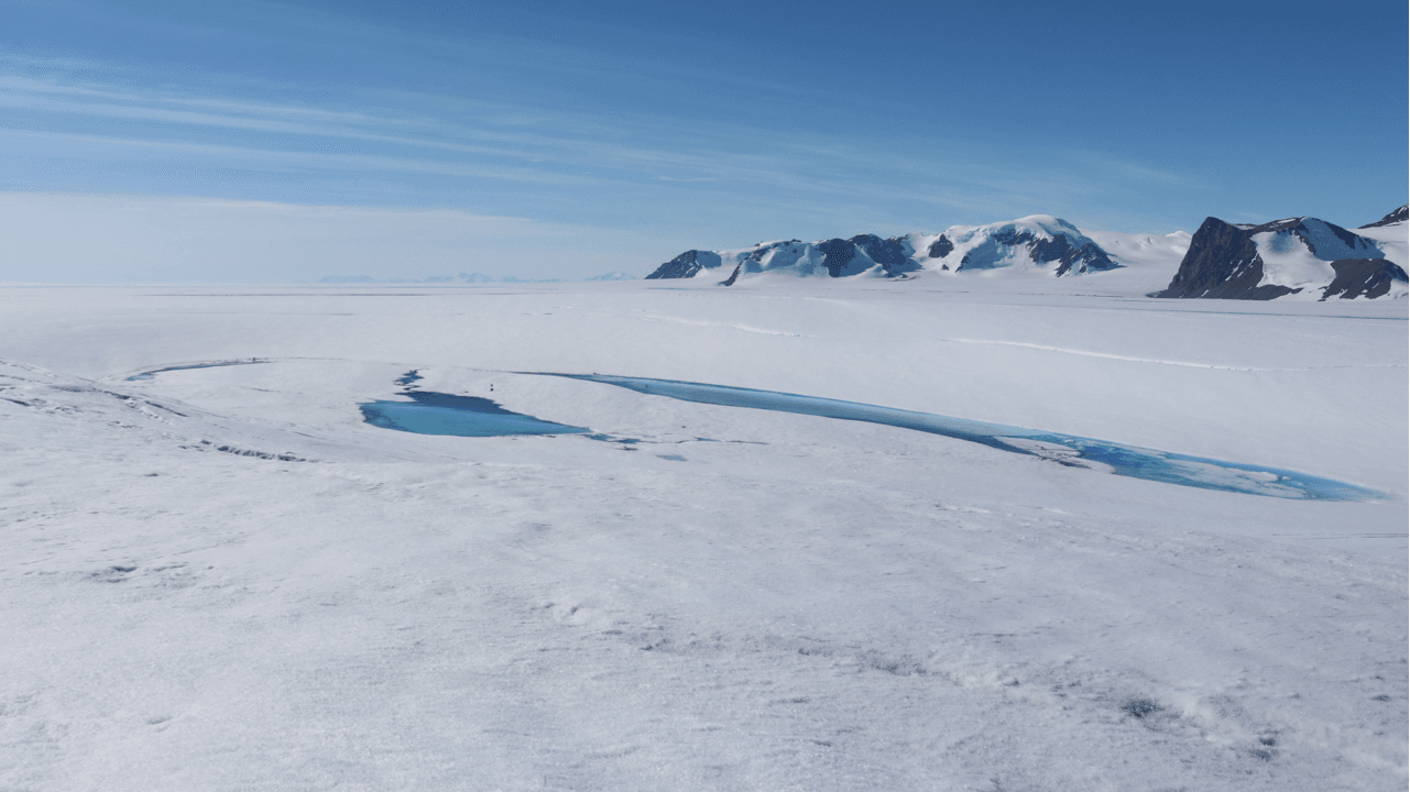 A meltwater lake on an icy surface with mountains visible in the background.