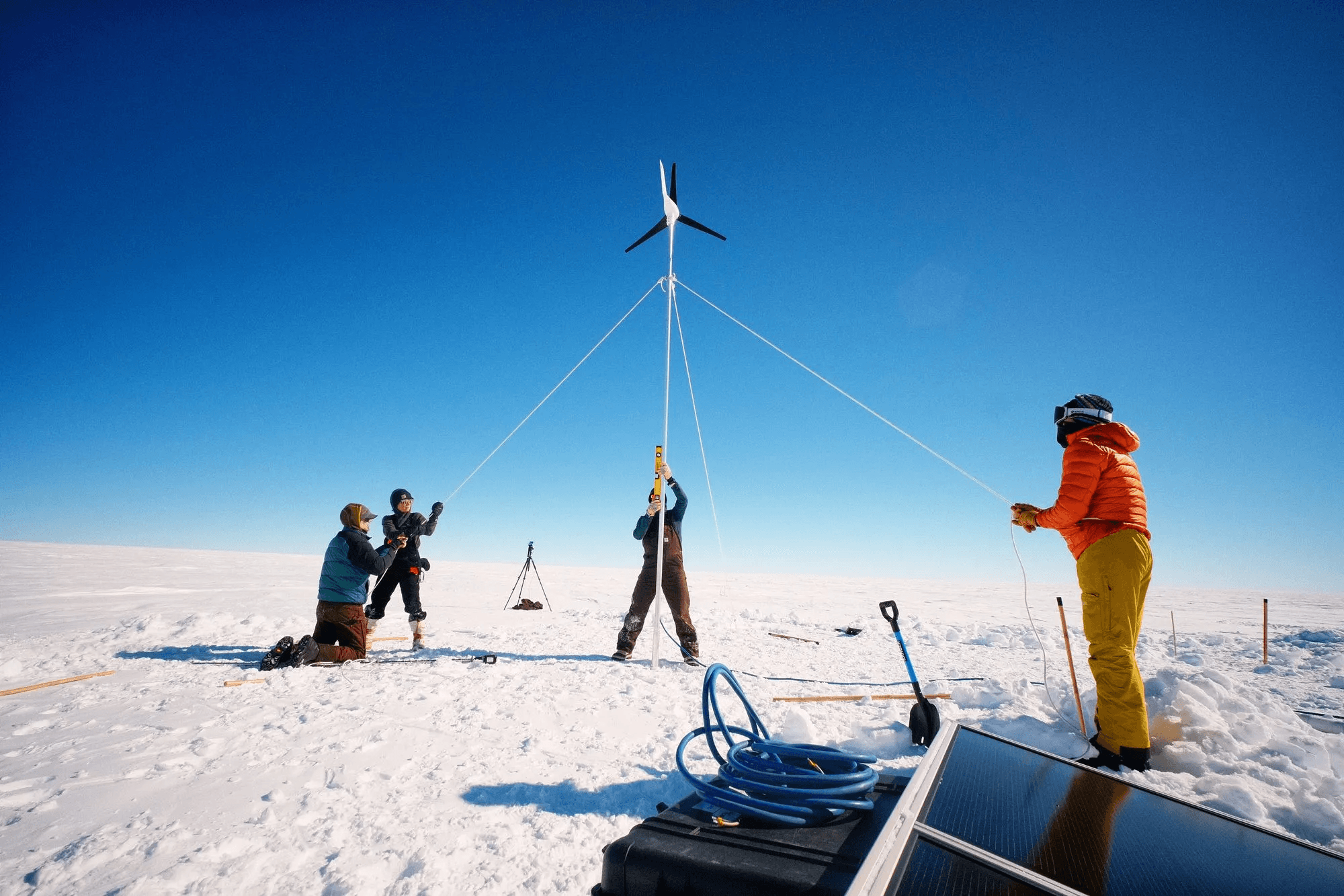 Four people setting up a wind turbine. Three people are holding lines, while one is holding the pole in the center.