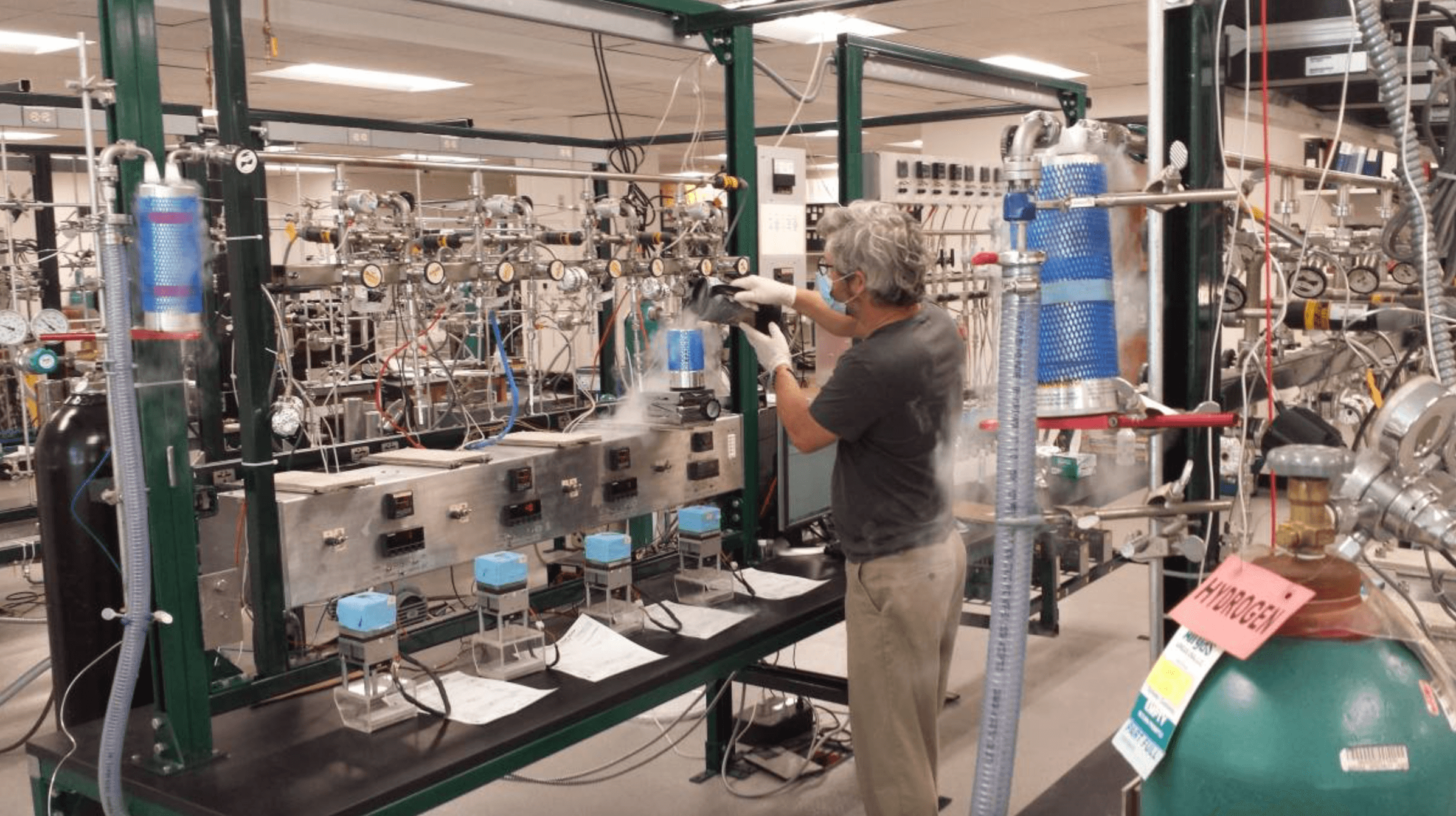 A person works on instruments in a lab while wearing gloves and a mask