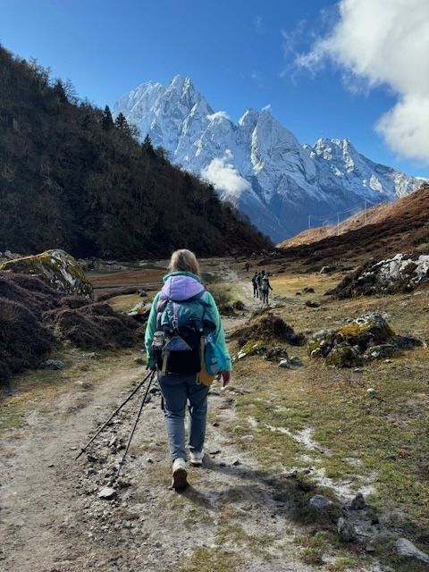 Two people in backpacking gear hiking down a trail toward tall mountains.
