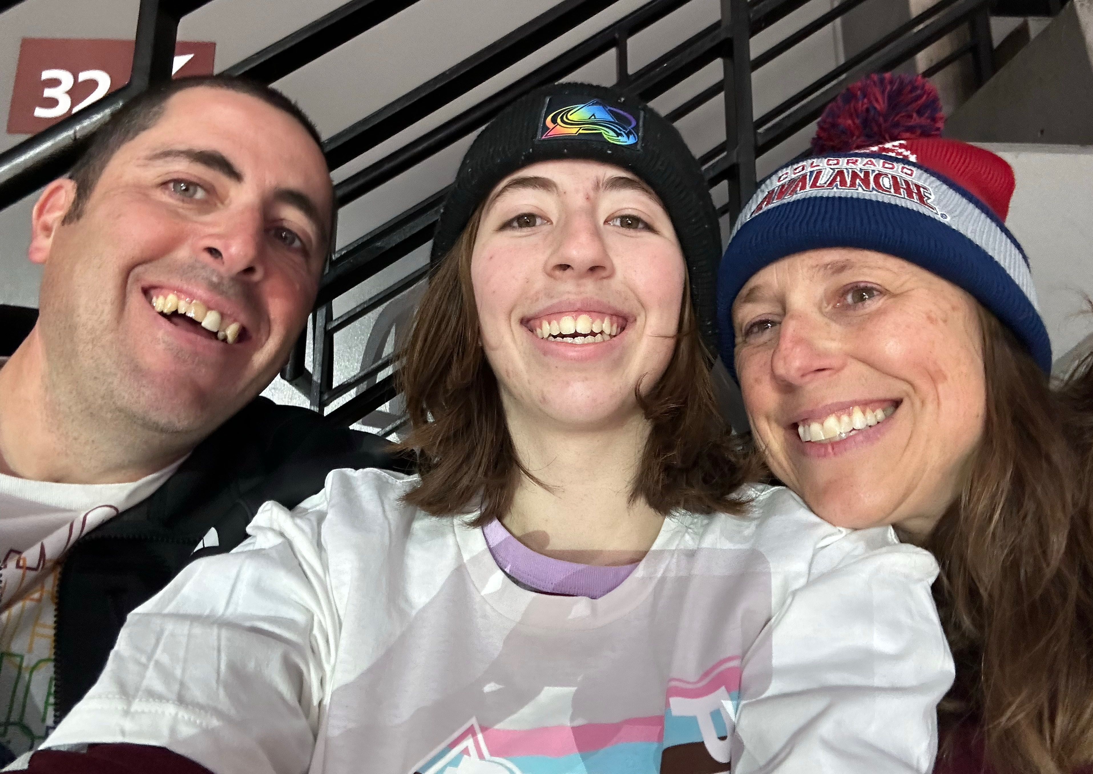 Three people smile for a photo together. Two are wearing winter hats.