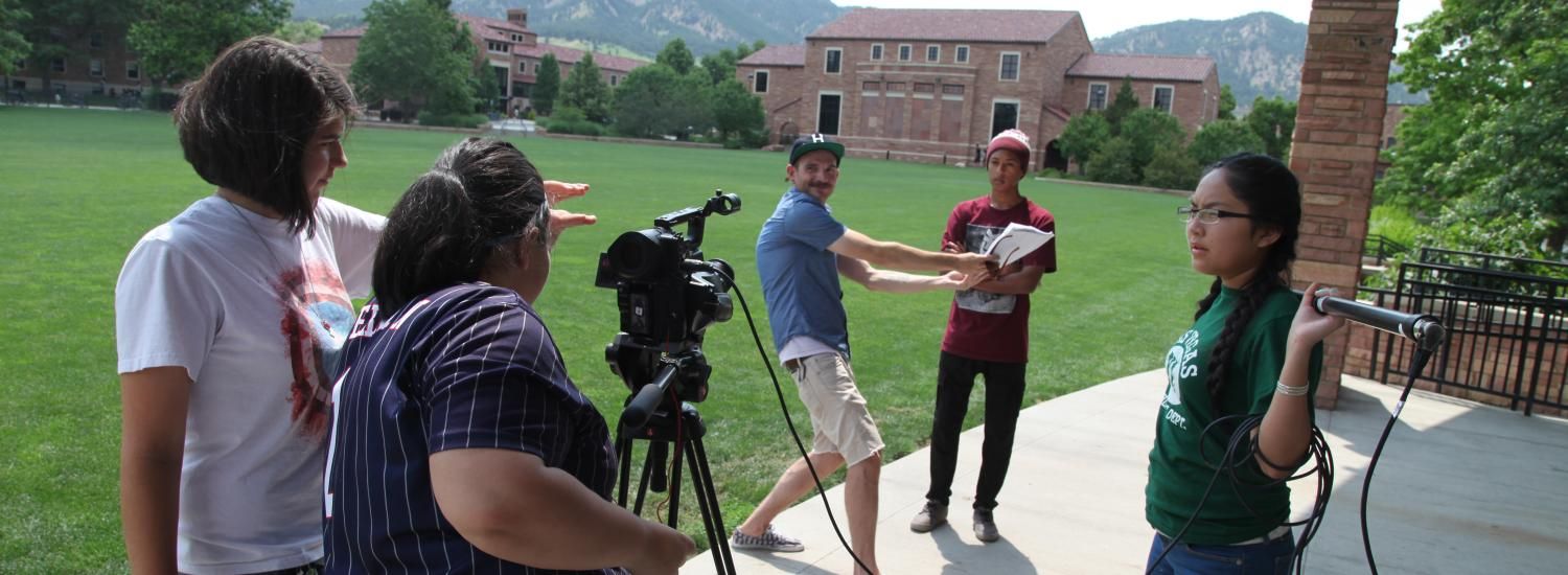 A mentor showing four students how set-up and film a video with a mountain visible in the background