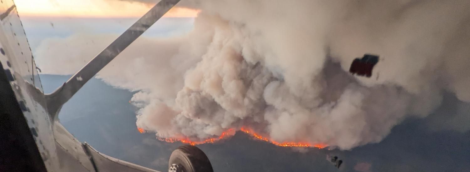 An aerial view of a large wildfire with a smoke plume. 