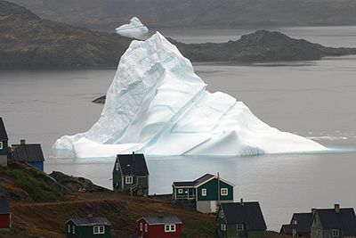 Large ice glacier in the ocean, houses in front on coast