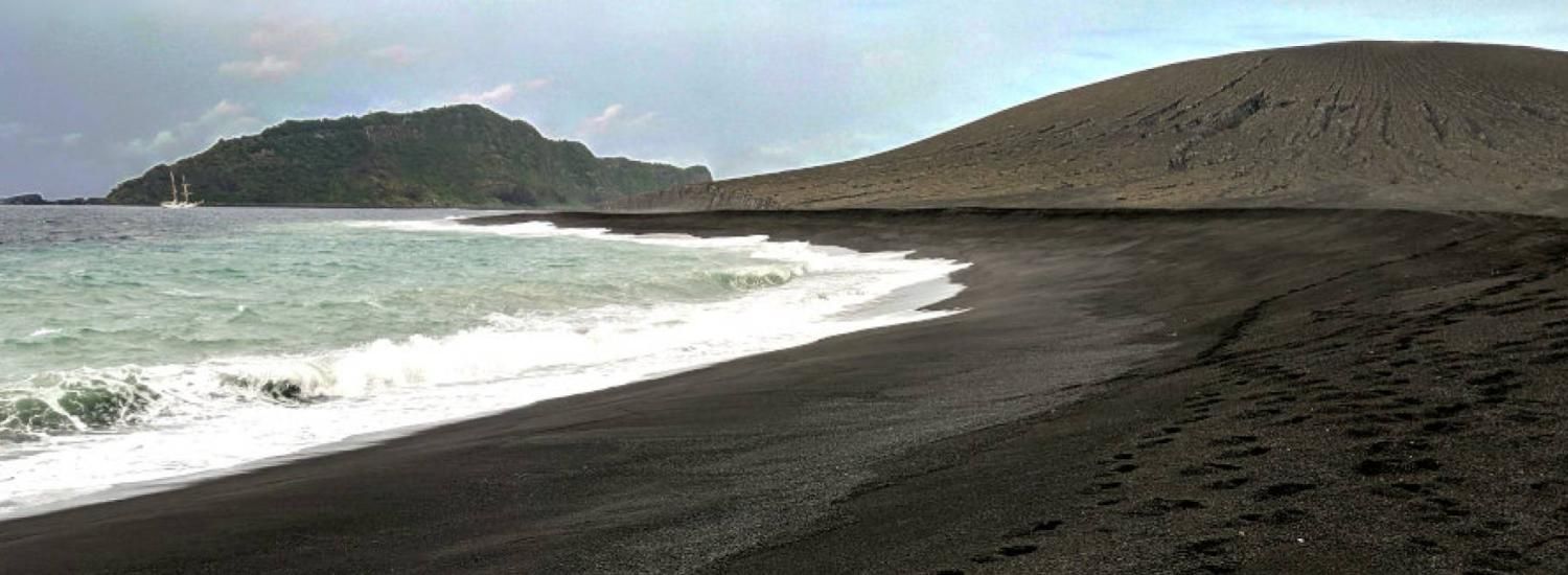black sand beach, hills in background, ocean waves