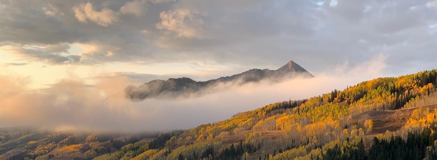 Clouds and fog move over mountains with yellow aspen trees