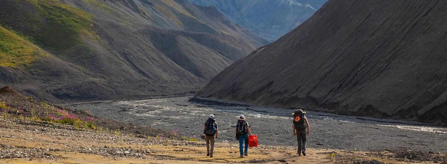 Three researchers walk down a riverbed in Alaska