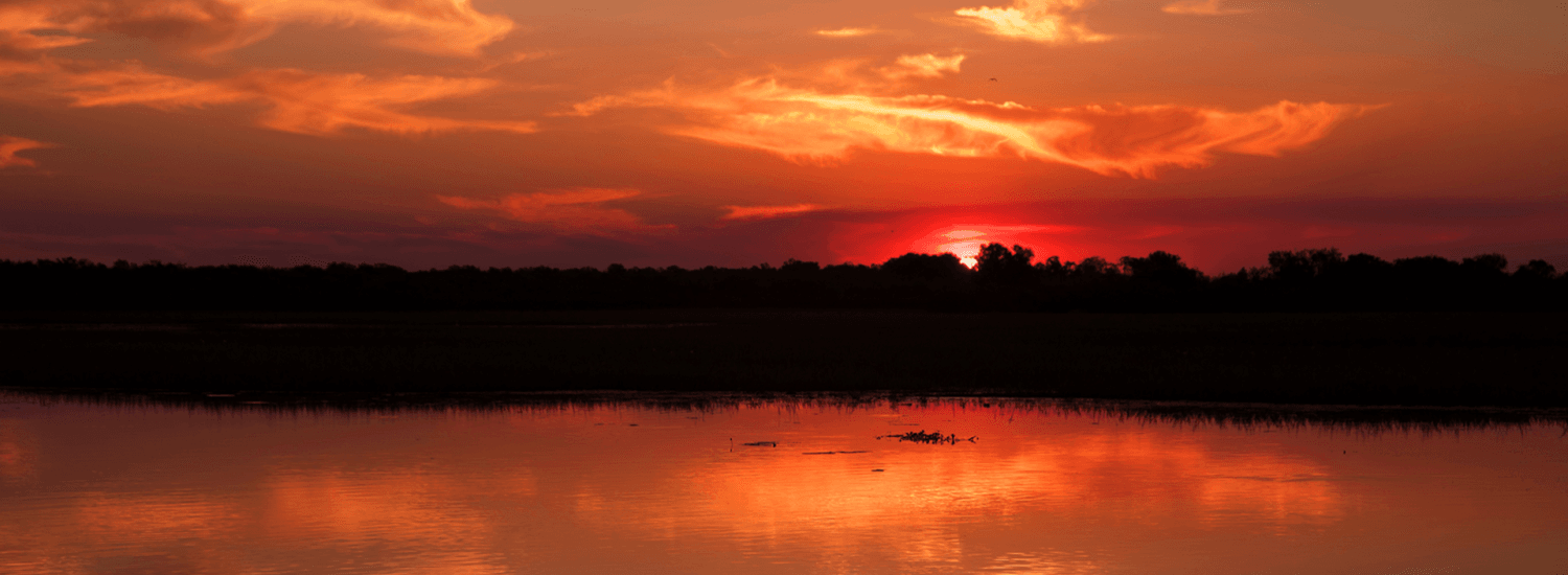 sun sets over a large body of water, casting sky in orange and red.