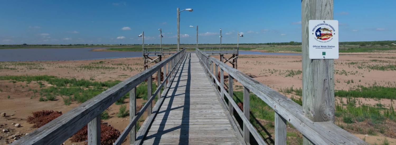 photo of pier surrounded by dry lakebed with lake in the background