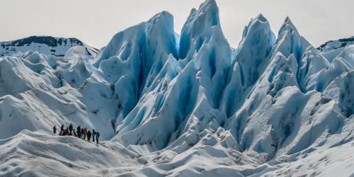 A group of people stand on a glacier with peaks that extend into the sky above them