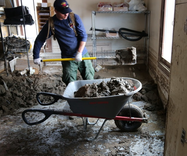 Shoveling mud out of the store room in Scotty's Castle Visitor Center. NPS.