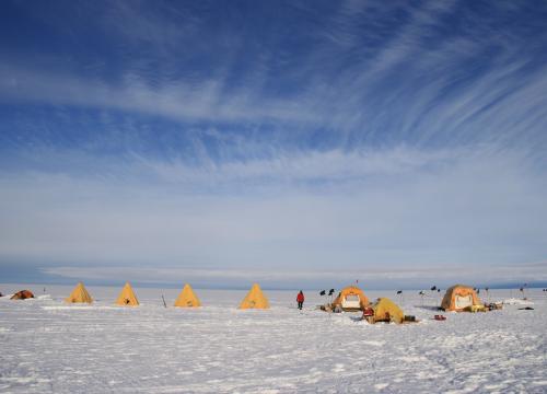 Bright yellow tents under a large blue sky on the very flat and snow covered Thwaites Glacier on Antarctica.