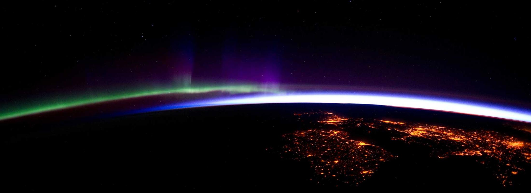 NOAA image of Earth's horizon from space you can see a green light on one side and a blue light on the other side of the horizon and some cities lit up from space on the Earth