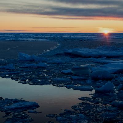 The sun sets over the ocean covered in sea ice.