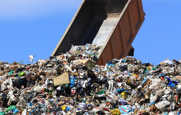 A large truck dumps trash into a landfill.